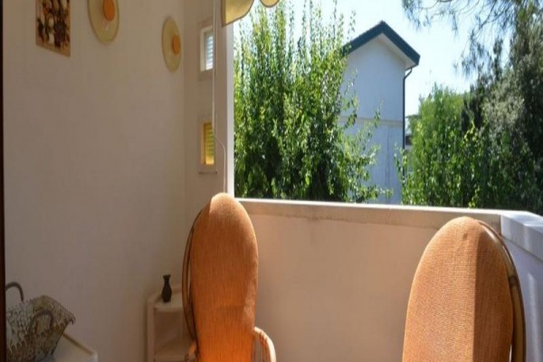 Dve ratanové kreslá na balkóne s výhľadom na stromy a budovu.